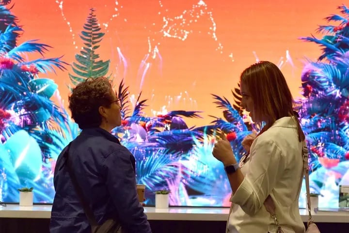 Two women are positioned in front of a large screen, appearing to collaborate or share ideas related to its content.