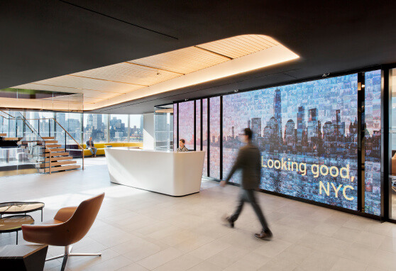 A large video wall dominates the lobby of a Hudson Yards corporate office, displaying high-resolution digital content that energizes the sleek, modern space. The vibrant visuals serve both aesthetic and informational purposes, creating a striking first impression for visitors and employees alike.