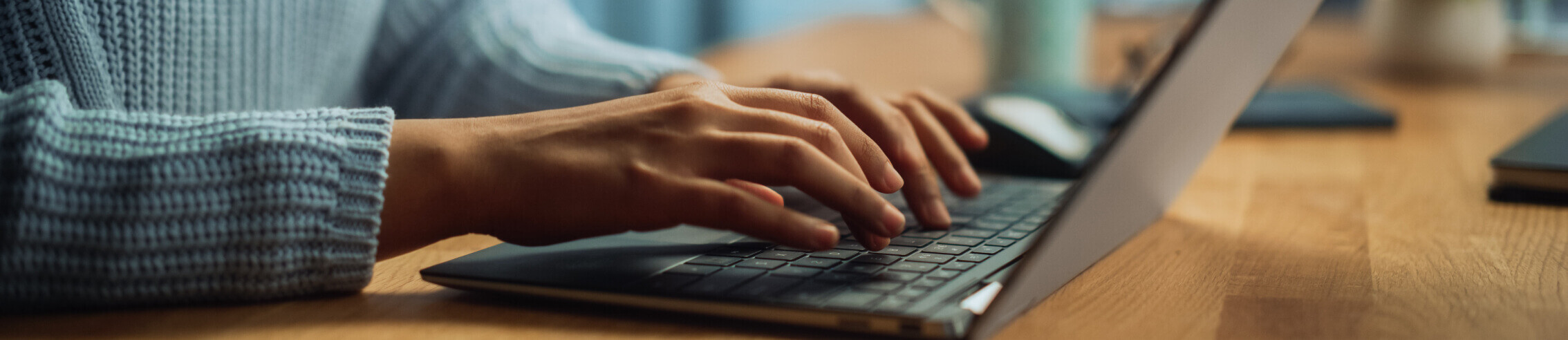 An individual types on a laptop in a well-lit workspace, focused on the screen as they work. The setting suggests productivity and concentration, with a clean desk and minimal distractions.