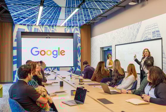 A boardroom with google on the screen and people sitting around the table