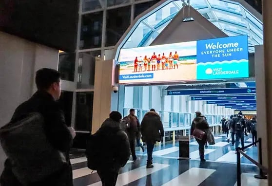 A commuter walks underneath a large digital advertising banner integrated into the building’s main concourse.