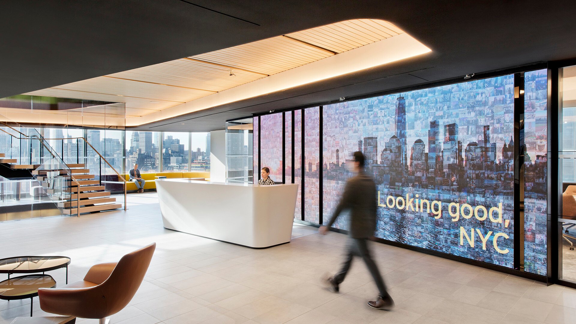 A digital installation set in the reception area of a modern office, which features a high-resolution digital wall that blends branding, ambiance, and a strong sense of place. The image mosaic of the city skyline formed from smaller photos suggests a celebration of community, people and company culture, all while welcoming visitors in a visually engaging and memorable way. It’s an elegant integration of media and environment.