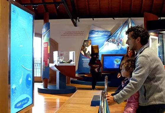 A father and his child playing a game at the Sailing Museum where they emulate steering a ship.