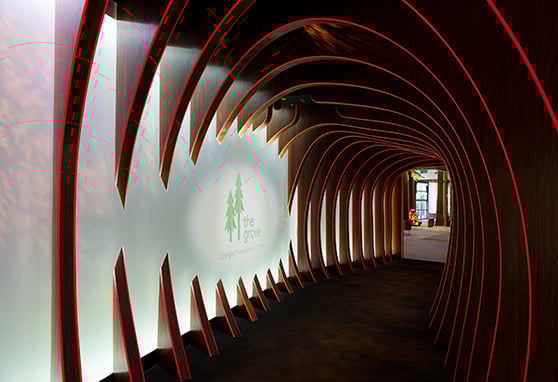 A futuristic tunnel of warm wood and glowing red light guides visitors into The Grove, Googles immersive Experience Center, blending nature-inspired design with cutting-edge tech ambiance.