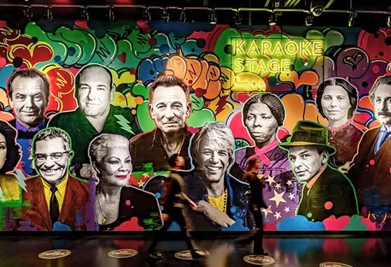 A guest walks past immersive digital displays honoring New Jersey icons, surrounded by vivid images and storytelling content.