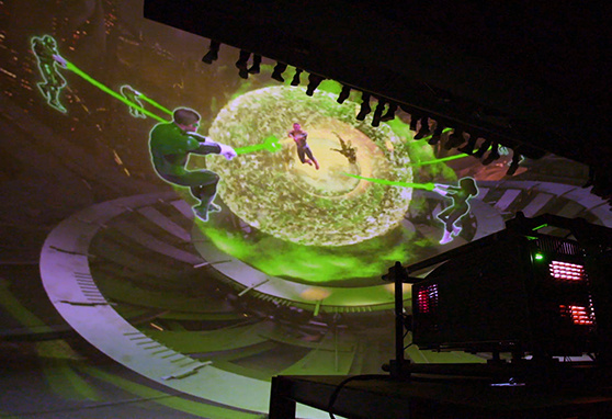 A high-powered projector displays a vivid, immersive scene on a domed screen, showing animated characters from the Green Lantern universe in a dynamic space battle