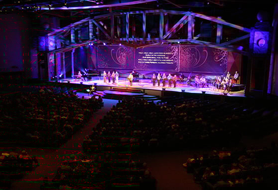 A large congregation gathers inside a modern auditorium for a worship service or performance.