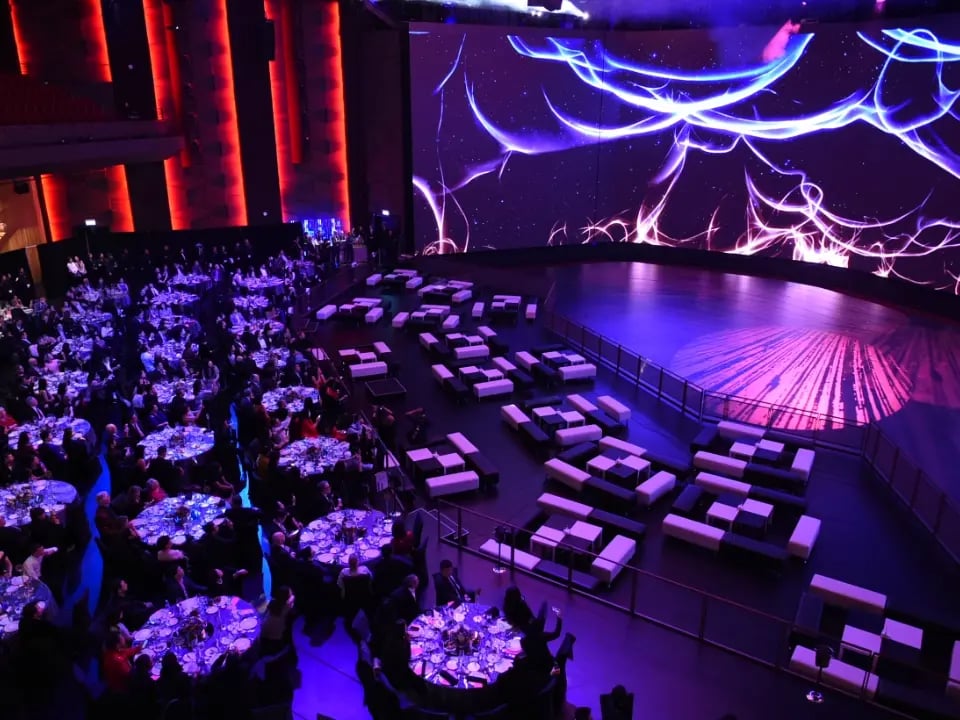 A large event with hundreds of guests sitting around circular tables while large LED walls set the stage for a night of entertainment.