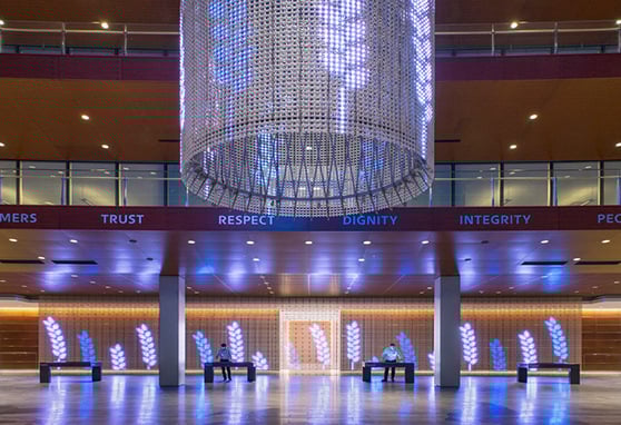 A modern corporate lobby glows with blue light and digital art, showcasing values like trust, respect, and integrity beneath a striking suspended installation.