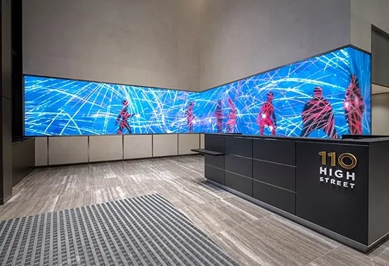 A sleek LED ribbon display runs along the interior of a corporate lobby, showcasing branded content and real-time data in a modern business environment.