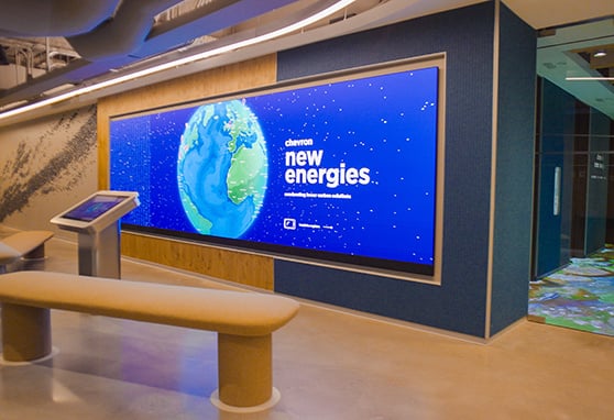 A sleek, modern space featuring an interactive display and large digital screen promoting Chevron New Energies, highlighting innovation in lower carbon solutions.