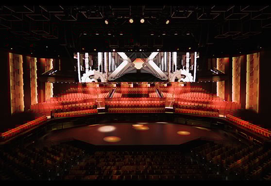 A state-of-the-art theater or performance venue with an immersive design. The seating is arranged in a semi-arena style, wrapping around the circular stage, which suggests it’s meant for performances that engage the audience from multiple angles—perfect for theater-in-the-round productions.