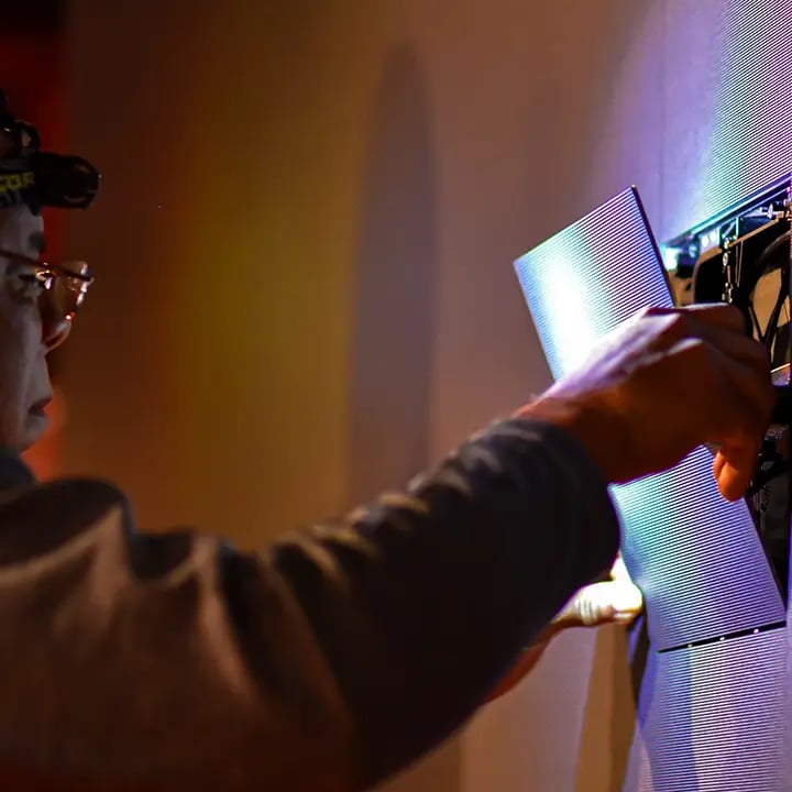 A technician carefully installs individual LED panels on a video wall, aligning them for seamless visuals and ensuring proper fit and connection.