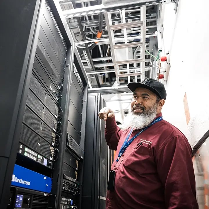 A technician services an AV rack filled with hardware components, performing routine maintenance or diagnostics to ensure smooth system performance.