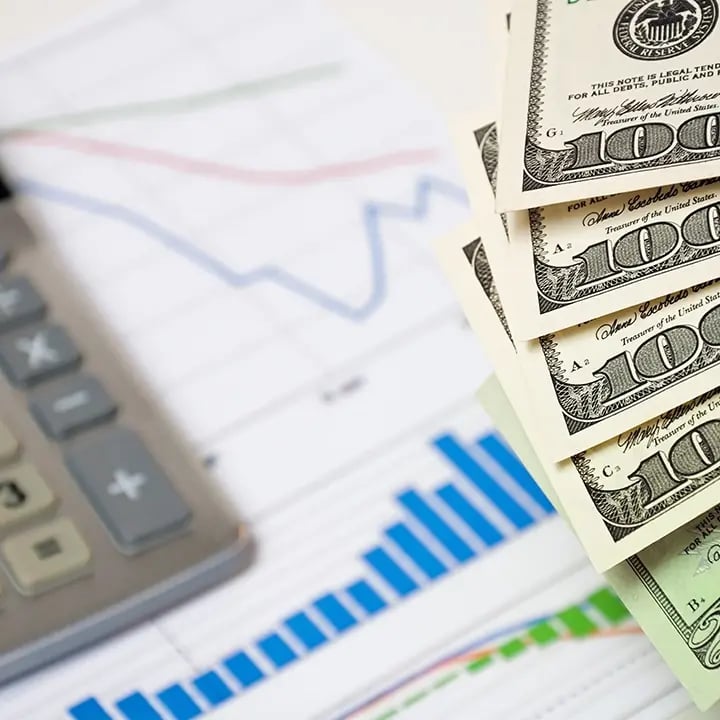 A calculator, hundred-dollar bills and statistic document underneath.