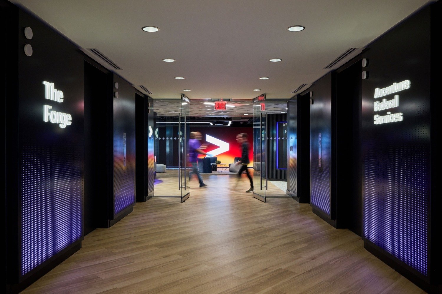 A hallway that is lined with walls displaying "The Forge" and "Accenture Federal Services".