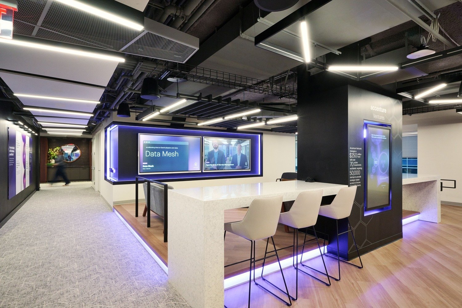 A sitting area with chairs, desks and two interactive LED screens on the wall.