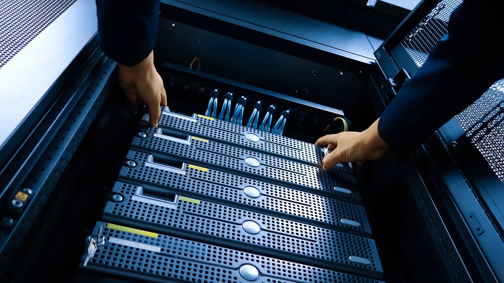 An AV technician installing media servers into a dark gray rack.