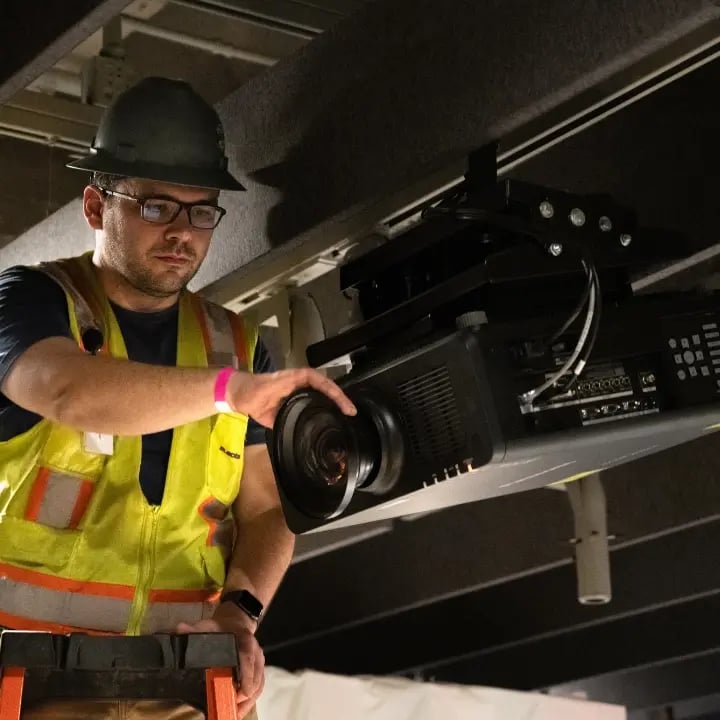 An Electrosonic technician checks a projector onsite to maintain image quality and system operation.