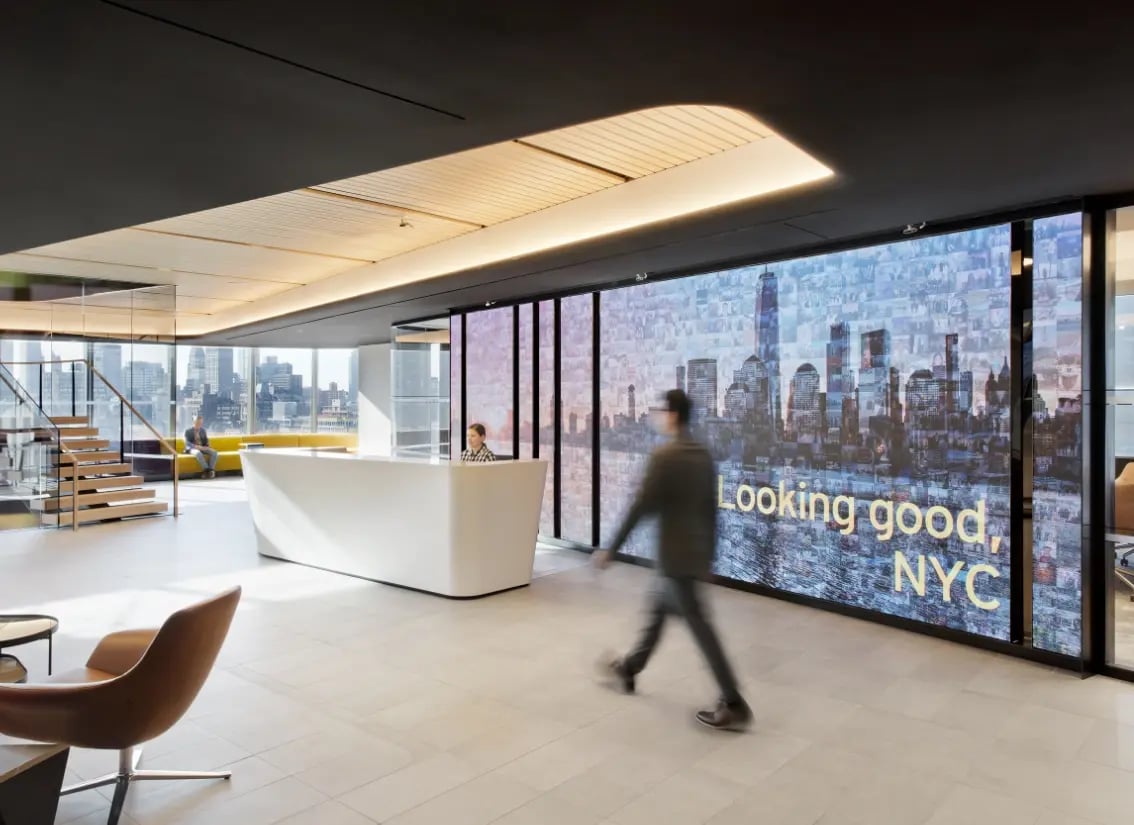 An employee walking through the lobby of a corporate HQ in New York, hes walking infront of a large LED wall.