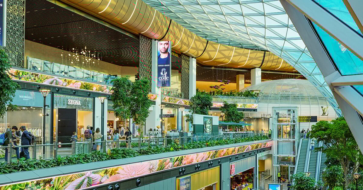 Travelers walking through Hamad International Airport's retail stores and between the large LED walls.