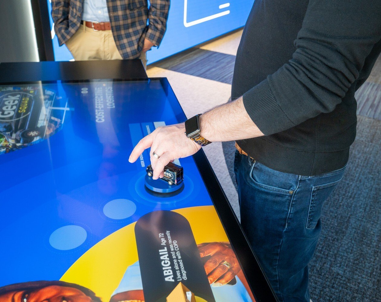 A person's hand holding a model truck on an interactive touch table.