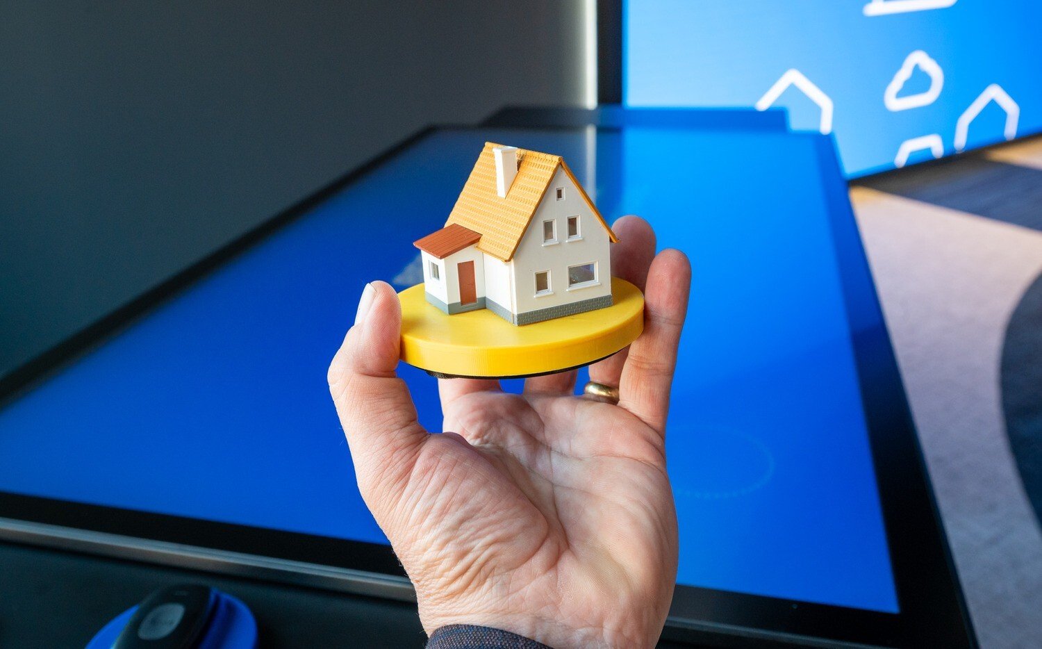 Hand holding a mini house in front of a touch table