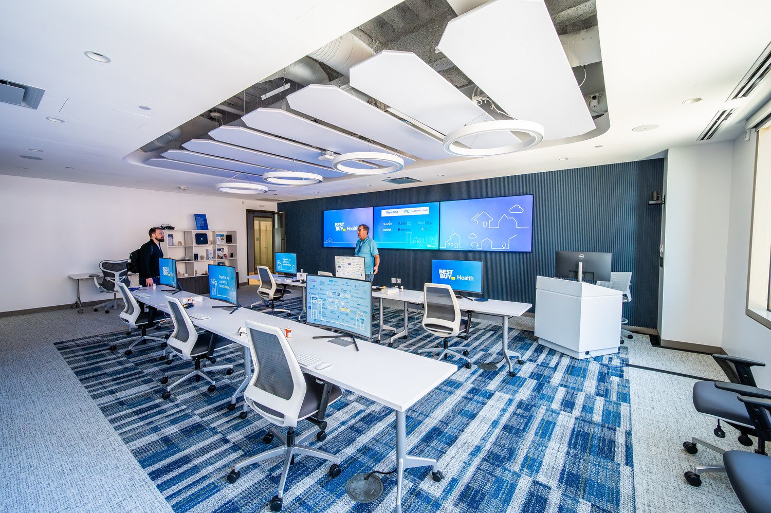 Corner back angle of a control room with 6 chairs, 6 monitors and three large monitors.