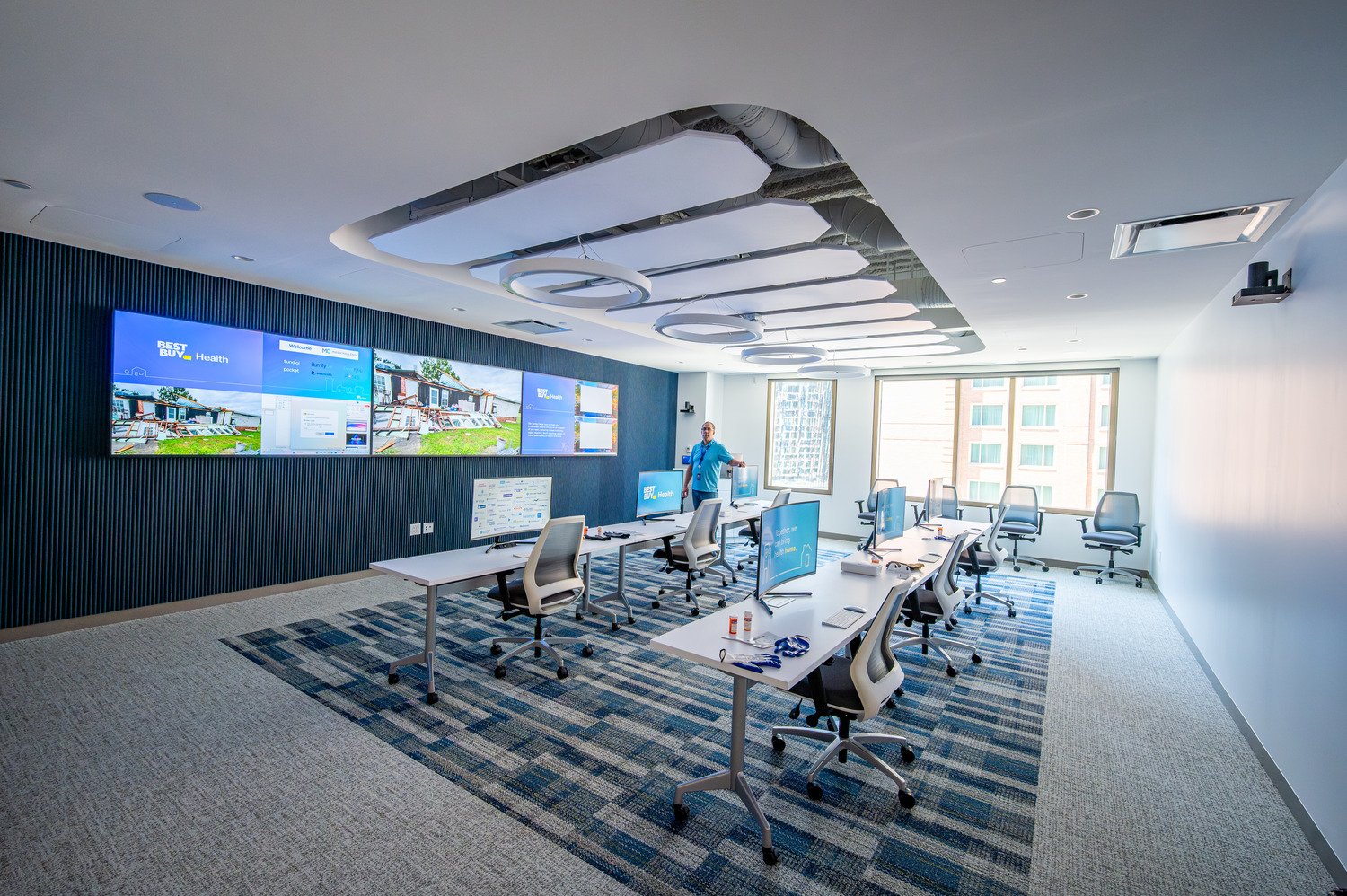 A control room with 6 chairs, 6 monitors and 3 large displays. 