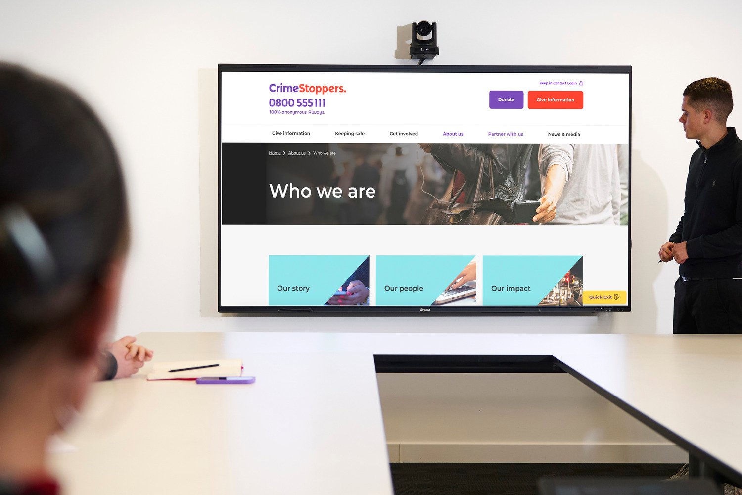A man looking at the display showing the Crimestoppers website with tables and chairs.