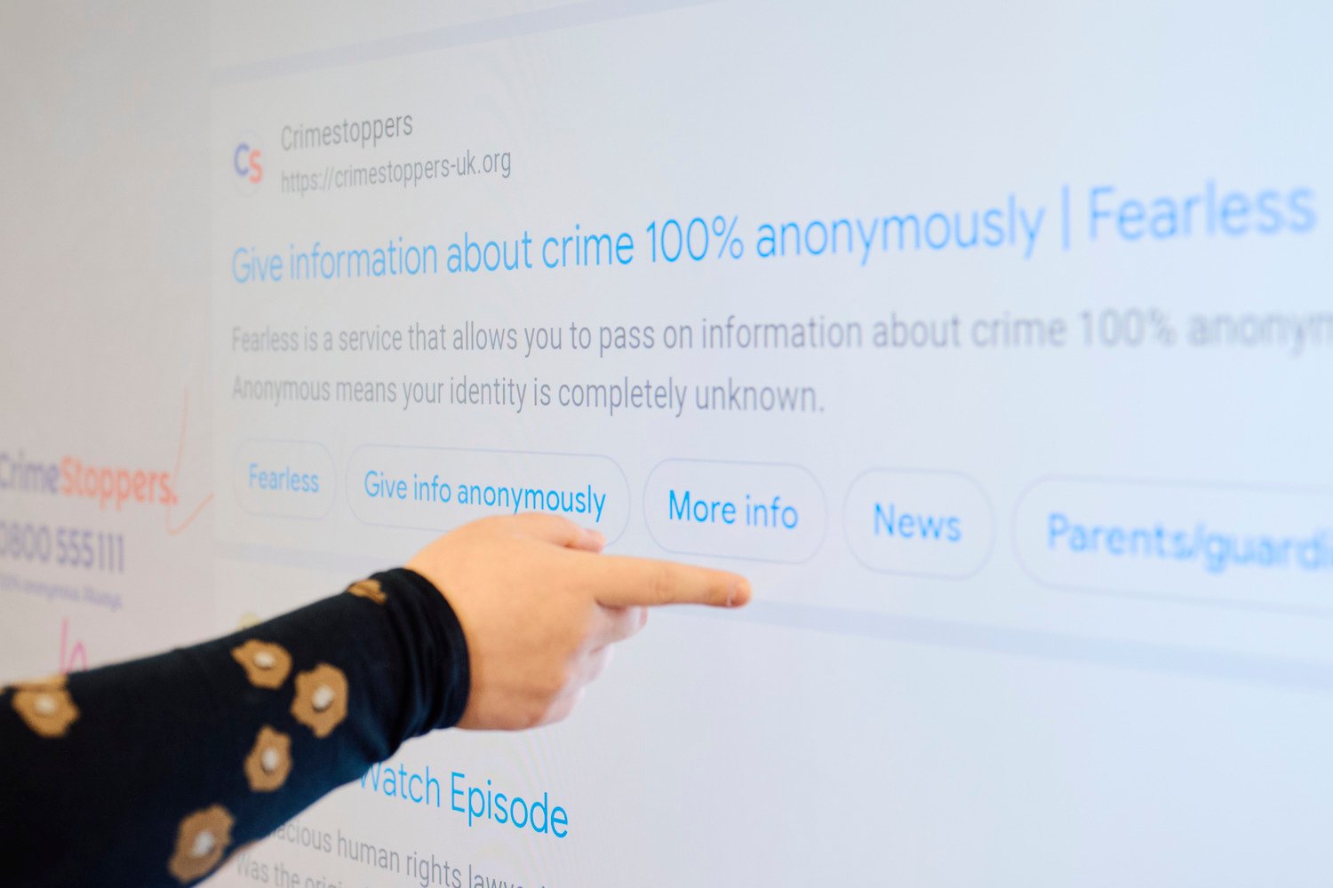 A hand touching the interactive display that shows the Crimestoppers website.