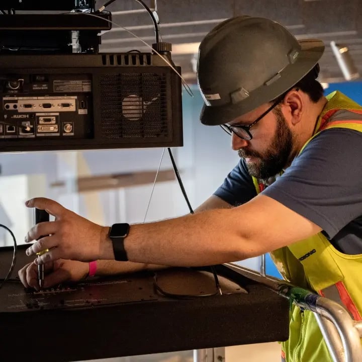 Certified Electrosonic technician troubleshooting and repairing a projector to ensure reliable operation.