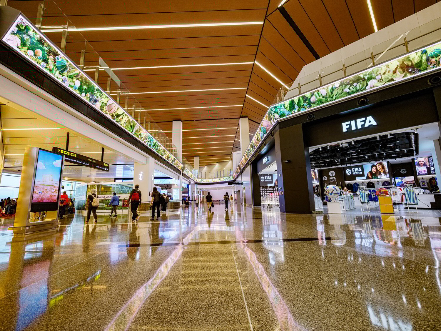 Hamad International Airport’s terminal with a massive LED wall that wraps around the space, displaying vivid, high-resolution digital content. The seamless integration of the screen enhances the terminal’s futuristic design and creates an immersive visual experience for travelers.