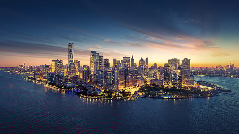 New York City at early dusk features a glowing skyline with the last light of day casting a soft hue over iconic skyscrapers. The city begins to light up as buildings and streets transition into the evening, creating a dynamic blend of natural and urban illumination.
