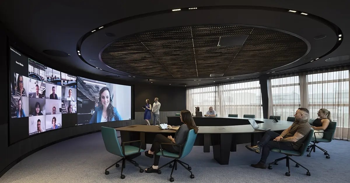 Employees engaged in a web conference within a large an immersive meeting room space.