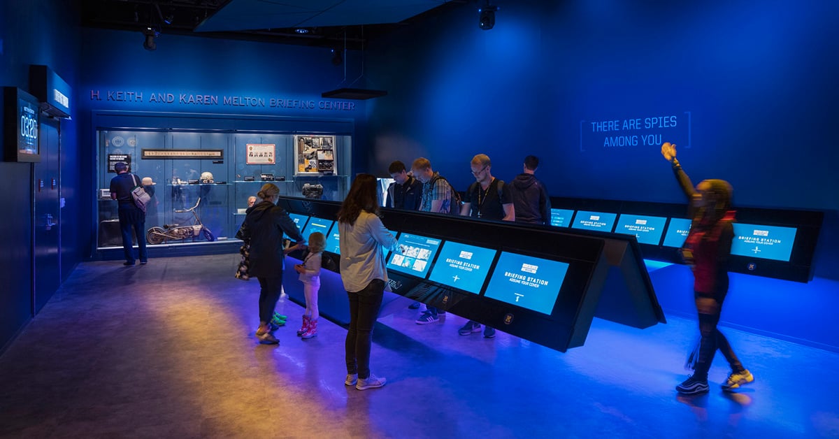 Group of visitors to a museum interacting with a series of touchscreens.