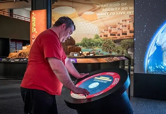 Guest at the Mars The Next Giant Leap exhibit at the Carnegie Science Center interacting with a touchscreen where they learn more about other planets.