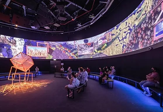 Guests sitting down in the Canada Pavilion at Expo 2020 Dubai, surrounding them is a large curved projection mapped experience.