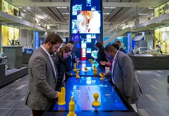 Guests to the Science History Institute all interacting with the object explorer, a touch table connected to a vertical video wall.