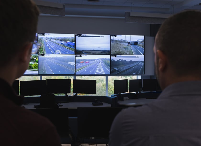 Two control room operators looking at traffic on a video wall at Highways England command.