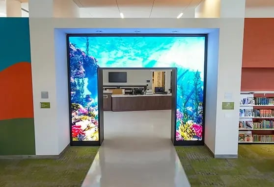 Inside the public library, a digital video wall presents local programming and educational content, enhancing the space’s civic and learning mission.