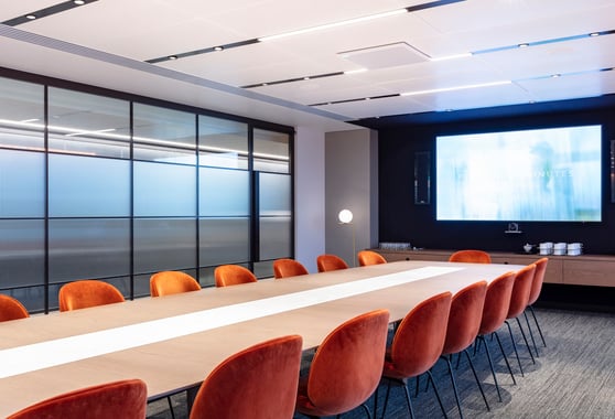 A boardroom with 16 chairs around a long table and a screen towards the end