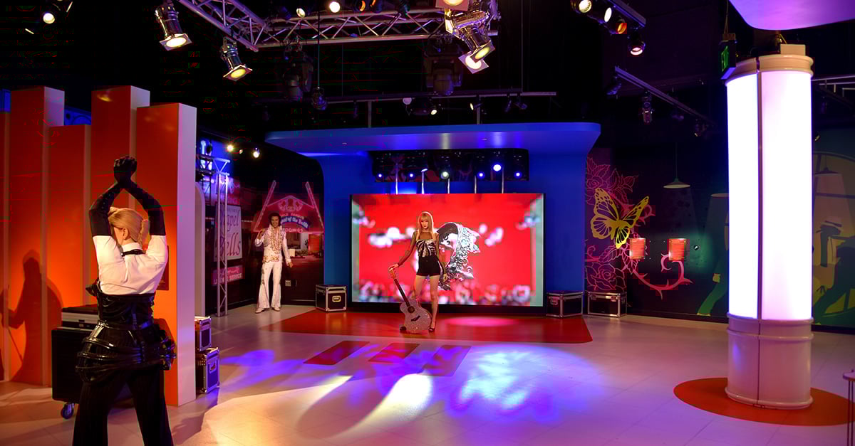 At Madame Tussauds in Orlando, a lifelike Taylor Swift statue stands in front of a massive LED wall displaying vibrant, dynamic visuals that enhance the immersive experience. The colorful digital backdrop adds energy and star power to the exhibit, drawing visitors into a pop-culture spectacle.