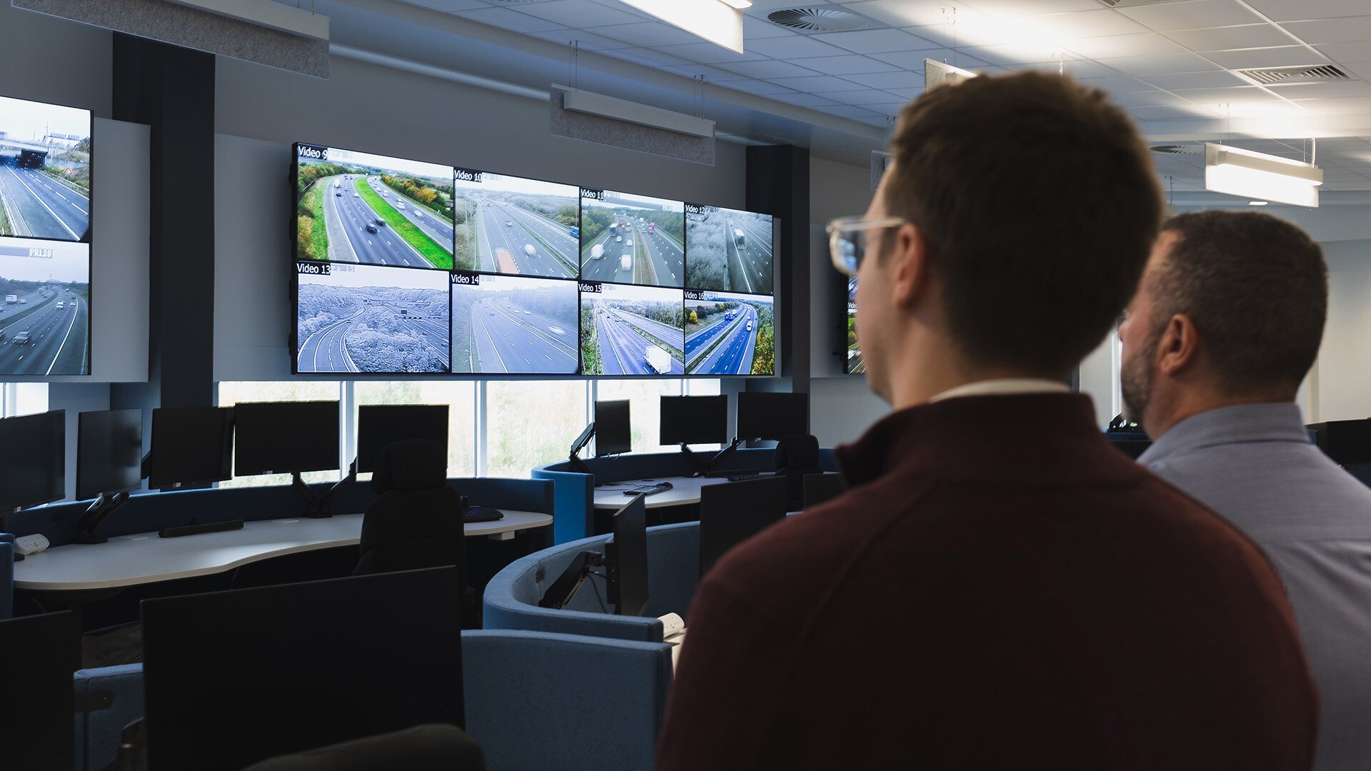 Two employees standing in front of a video wall at the National Highways North-East Regional Operation Centre.