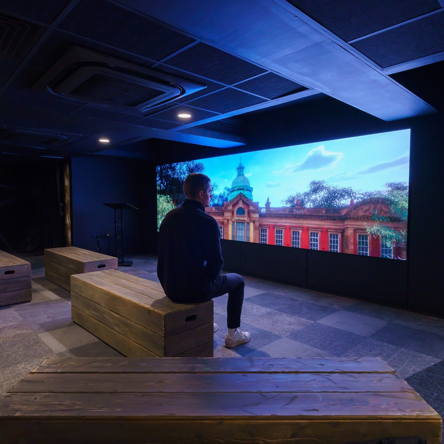 A man watching a video wall with Durham Miners Hall on it.