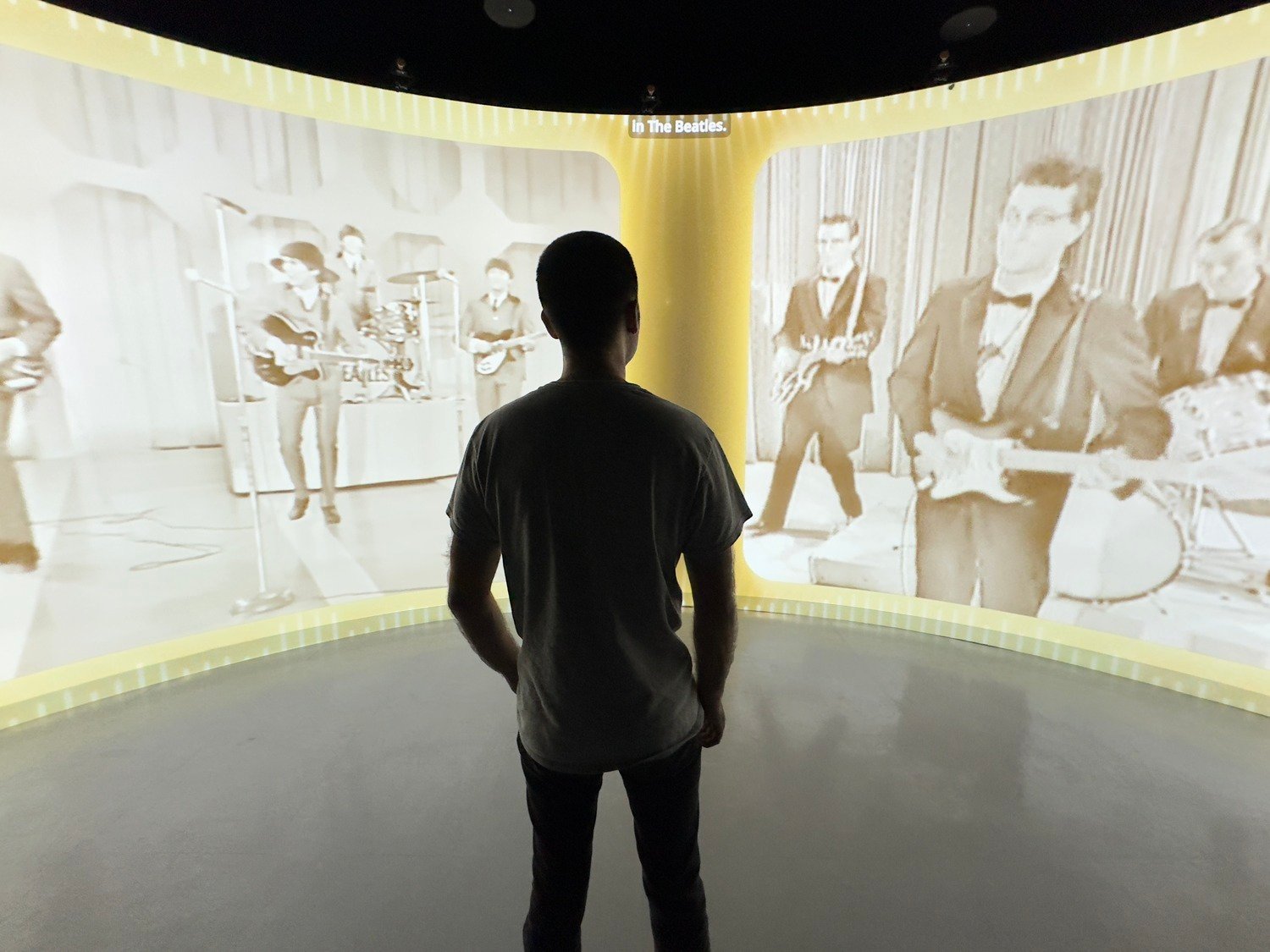 A guy looking at the curved projection wall watching the media about American music history.