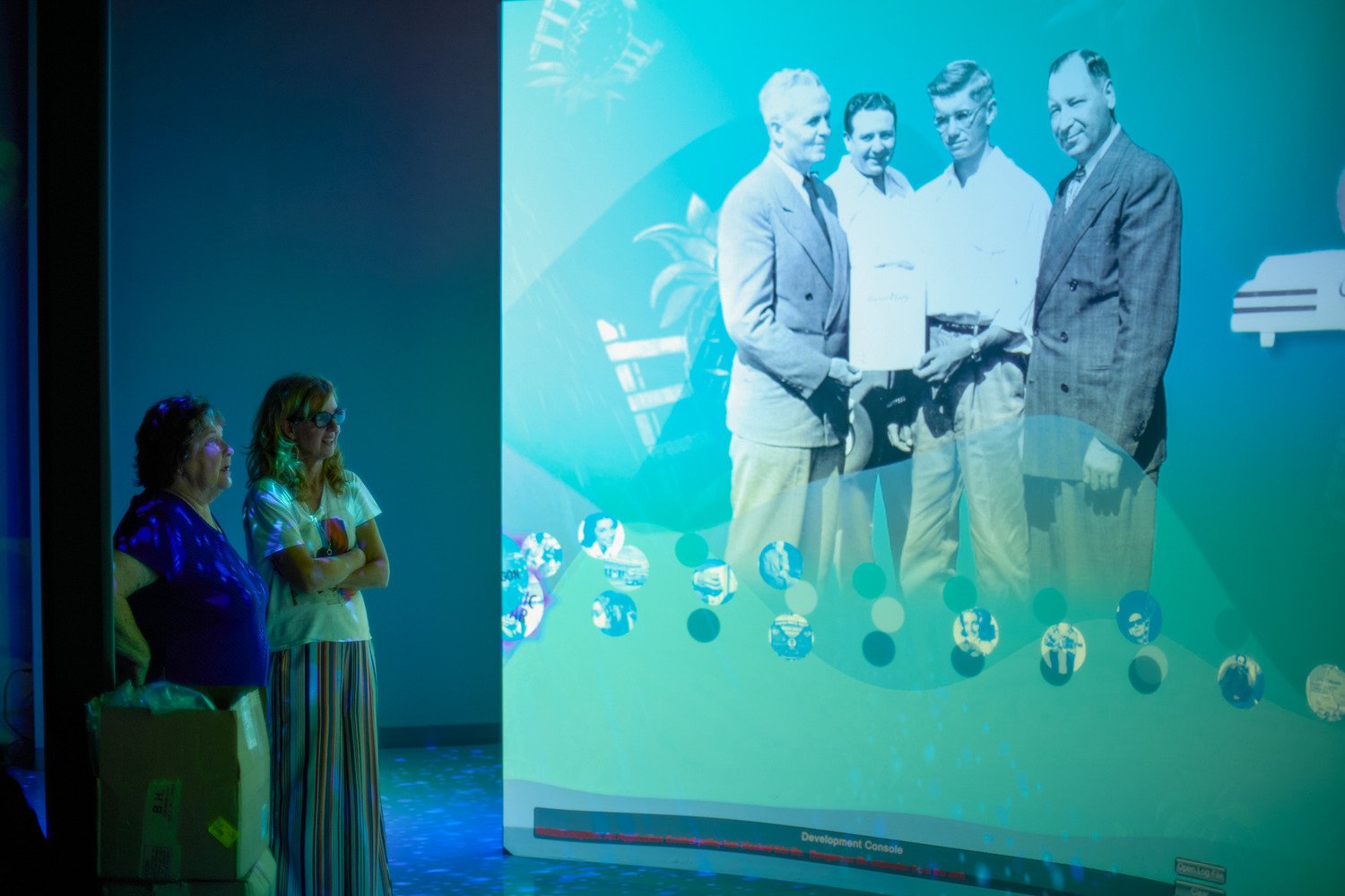 Two women looking at a curved media projection wall watching history about music legends.
