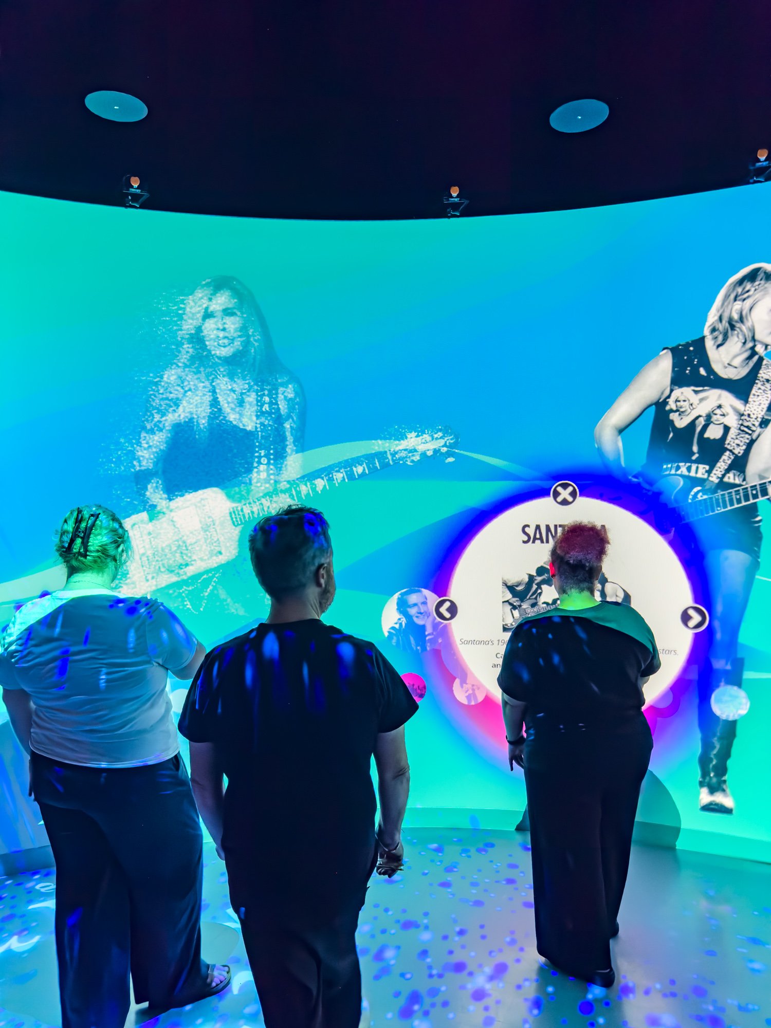 Three people looking at the media on a curve projection wall.