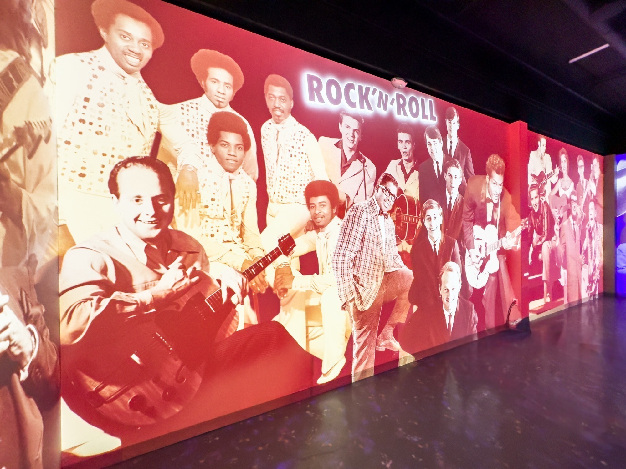 A wall that has projected media of music legends in a red filter.