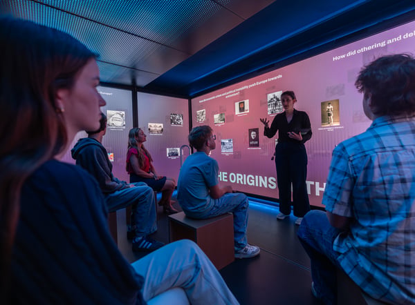 People viewing media with woman talking at front of room.
